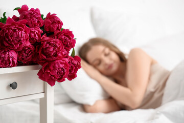 Beautiful young woman and bouquet of peony flowers in bedroom