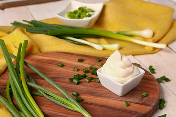 Bowls of tasty sour cream and sliced green onion on white wooden background