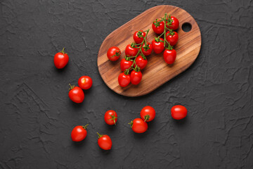 Wooden board with fresh cherry tomatoes on black background