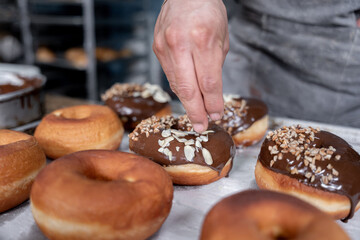 A young Hispanic baker is dropping almond toppings on a chocolate donut