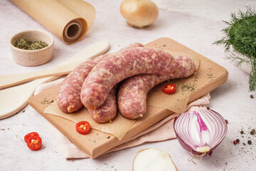 Wooden board with raw homemade sausages on light background