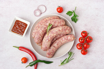 Plate with raw homemade sausages and sauce on light background