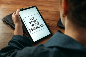 A woman holds a tablet in her hands on the screen of which it is written - We Want Your Feedback