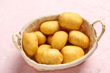 Fototapeta na wymiar Wicker basket with raw baby potatoes on pink background