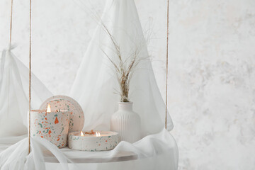 Holders with burning candles on hanging shelf near light wall in room, closeup