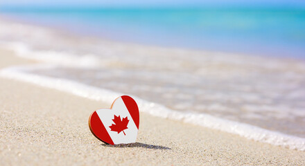 Flag of Canada in the shape of a heart on a sandy beach.