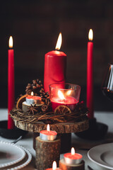 Rustic table decor for Christmas or New Year family dinner. Centrepiece with red candle, dry orange, cone, cinnamon, anise. Zero waste eco-friendly home. Cozy atmosphere, dark background. Close up