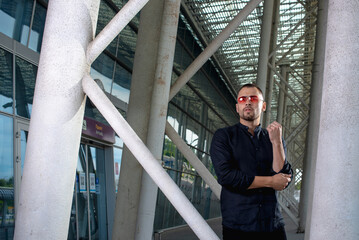 a stylish man in light pants and a black shirt against the background of empty walls holds glasses in his hands and looks away angrily