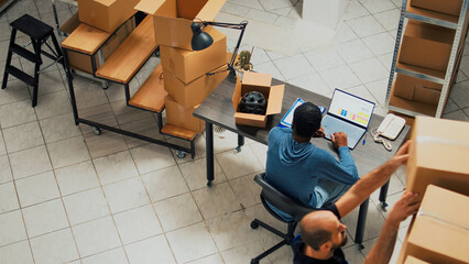 Male entrepreneur analyzing quality of products in storage room, preparing merchandise order for shipment. Young man putting supplies and goods in carton packages to ship to customers.