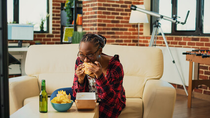 Cheerful person eating hamburger from fast food takeout, enjoying meal with burger and fries while...