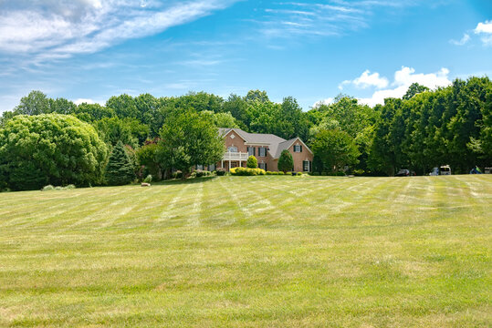 Landscape with a beautiful house, with a well-groomed and landscaped yard. Big lawn under blue sky.