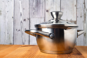 Stainless steel saucepan with a glass lid on a wooden table. Side view.