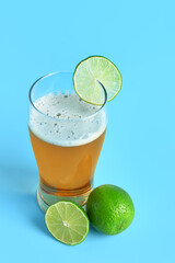 Glass of cold beer with lime on blue background