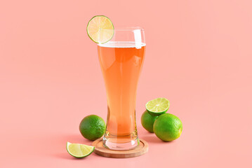 Glass of cold beer with lime on pink background