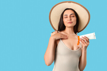 Young woman applying sunscreen cream on blue background