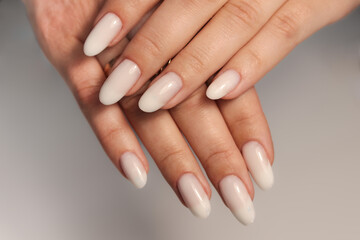 Nude manicure. Long almond shaped nails. Nail design. Manicure with gel polish. Close-up of the hands of a young woman with a gentle nude manicure on her nails. Bright nails with gel polish.