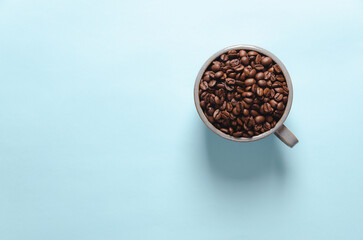 Coffee beans in a cup on blue background, top view.