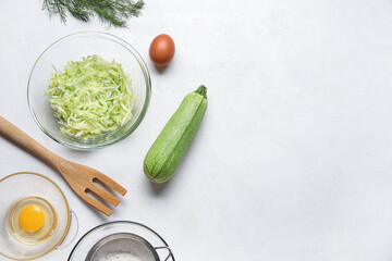 Bowl with grated zucchini and ingredients for preparing fritters on light background