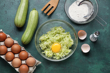 Bowls with grated zucchini, flour and eggs for preparing fritters on green background