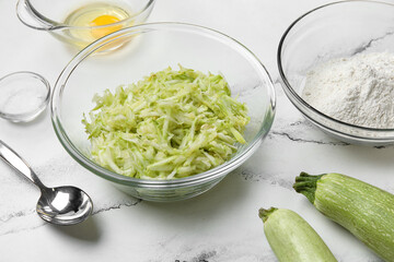 Bowls with ingredients for preparing zucchini fritters on white marble background