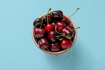 Bowl with sweet cherries on blue background