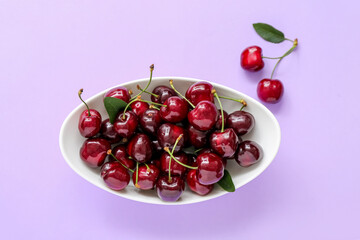 Bowl with sweet cherries on lilac background