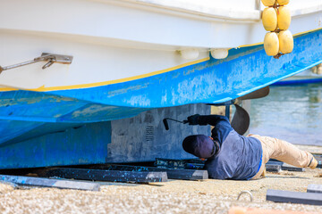 陸揚げした漁船の船底を塗装する人