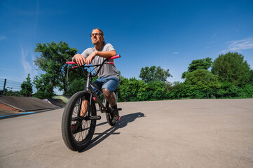 An urban tattooed mature guy is posing on his bmx bike in a skate park.