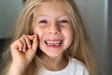 a little blonde girl in the bathroom looks into the camera, smiles and shows a fallen milk tooth, close-up