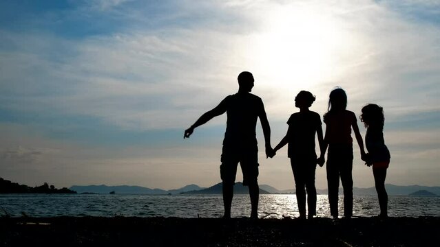 Silhouette of a family of tourists. A man holds a woman's hand, a woman holds children on the beach.