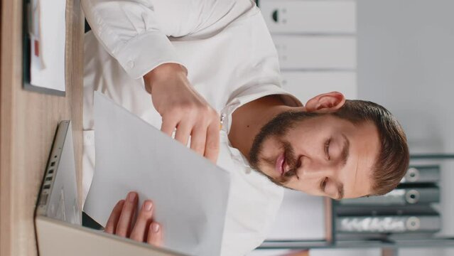 Businessman ceo reading business contract, planning project, analyzing resume, satisfied with good paperwork results. Man at office looking at camera talking, online conversation interview. Vertical