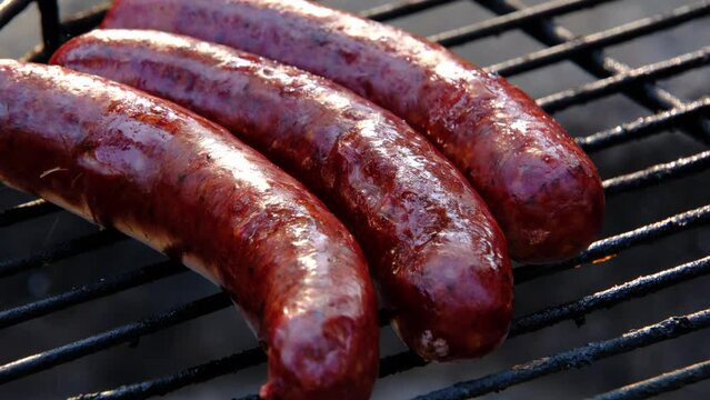 Close up of smoked sausage bursting with fat while being overcooked on the grill over fire pit.