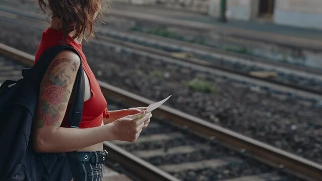 Portrait of young asian girl with backpack standing on platform or railway station with ticket in hands. Woman going on trip or travel by train. Passenger awaiting imminent departure on vacation.