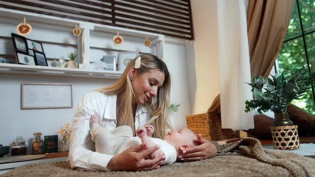 Beautiful blonde woman embracing her newborn son lying on the plaid. Mother calming the kid who waves little feet and hands touching mom's hair.