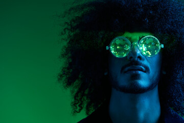 Fashion portrait of a man with curly hair on a green background with sunglasses, multinational, colored pink light, trendy, modern concept.