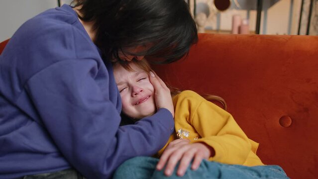 Portrait of upset offended child little girl kid crying with tears flowing down on her cheek, toddler lies on mother at home. Mom hugs, embrace, takes pity on her daughter. Quarrel, bullying at school