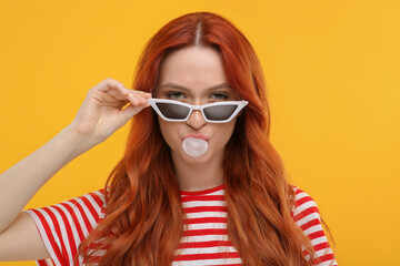 Beautiful woman in sunglasses blowing bubble gum on orange background