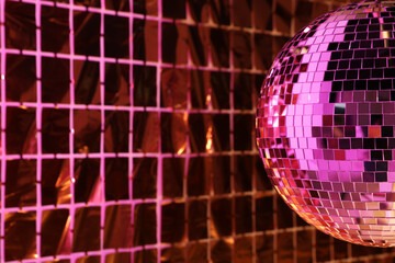 Shiny disco ball against foil party curtain under pink light, space for text