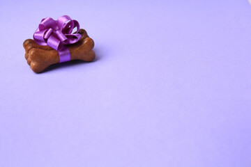 Bone shaped dog cookies with beautiful bow on purple background, space for text
