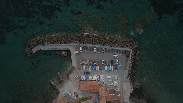Port de Valldemossa, Mallorca, aerial view of a small harbor in a coastal village, parked cars and boats, clear water with rocks and a reef, Mediterranean coastline, drone flight above the sea, travel