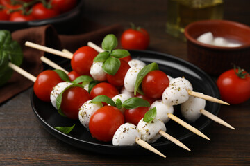Delicious Caprese skewers with tomatoes, mozzarella balls, basil and spices on wooden table, closeup