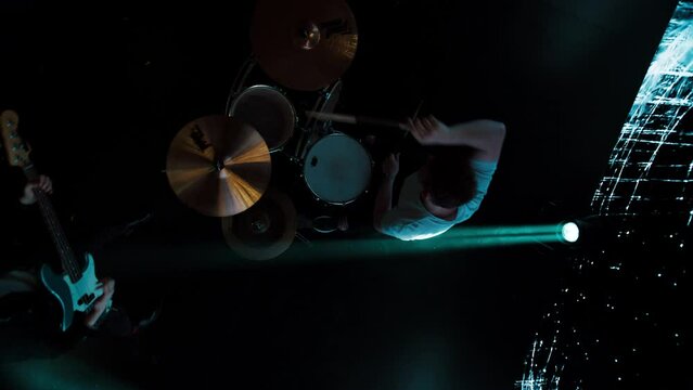 Jib shot of a drummer performing his solo during rock band concert on stage of a large venue, surrounded by bright flashing stage lights