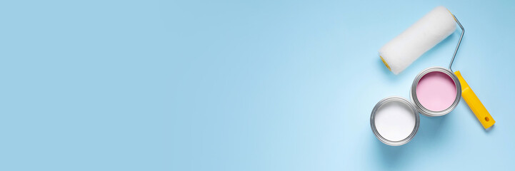 Cans with different paints and roller on light blue background, flat lay. Banner design with space for text