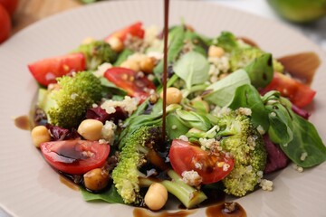 Pouring balsamic vinegar onto tasty salad in plate, closeup