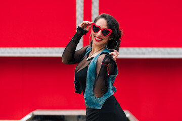 retrato de bella mujer latina con maquillaje jugando con sus lentes rojos al aire libre en un fondo...