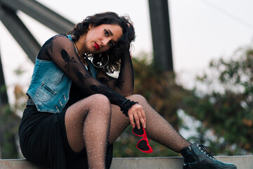 bella mujer latina sentada en la calle en estructuras metálicas, estilo 80s 90s en un parque al...