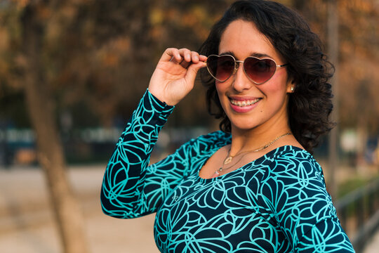 retrato de bella mujer latina con lentes en un parque estilo 80s 90s con vestido azul, muy alegre y feliz.