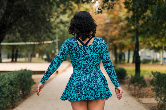 hermosa mujer latina andando en patines estilo 80s 90s con vestido azul de espaldas en un parque.