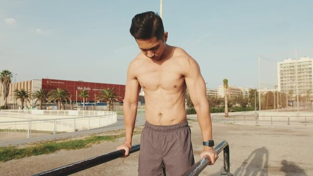 Young man doing push-ups on parallel bars on a sports ground by the sea