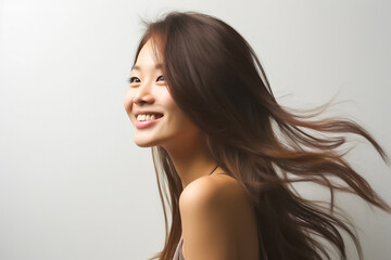 Fototapeta premium Charming Asian teenager with long hair blowing in the breeze exudes positivity with a bright smile on a white background.